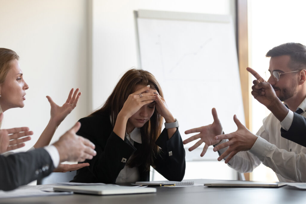 Four employees arguing during a meeting, exhibiting common communication issues in the workplace