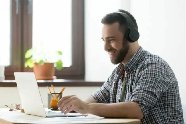 bearded man with headphones smiles while watching product training on laptop