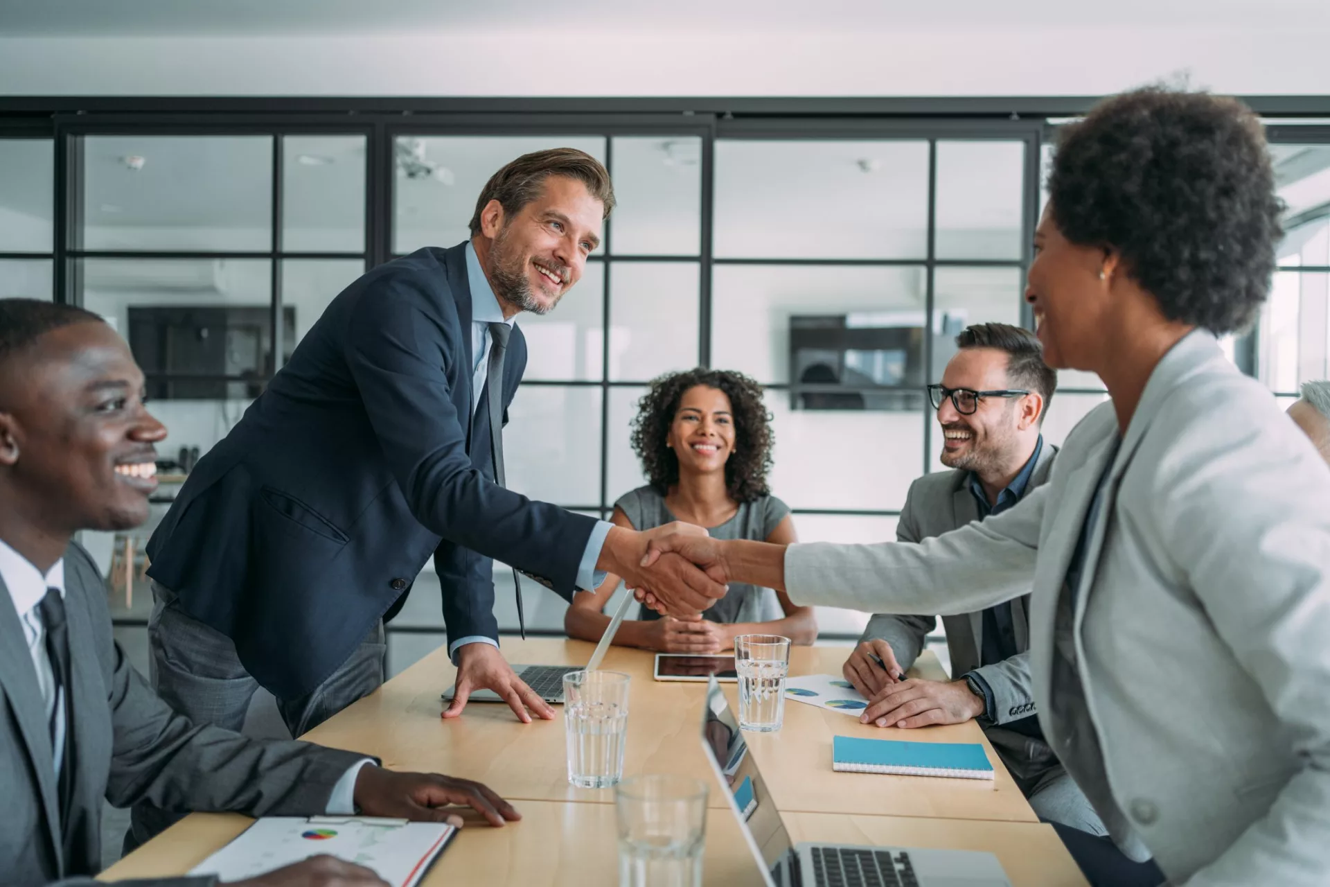 two businesspeople shake hands across conference room table