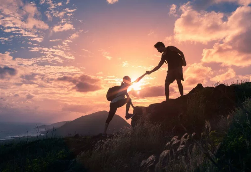 hikers helping each other up mountain representing knowledge sharing