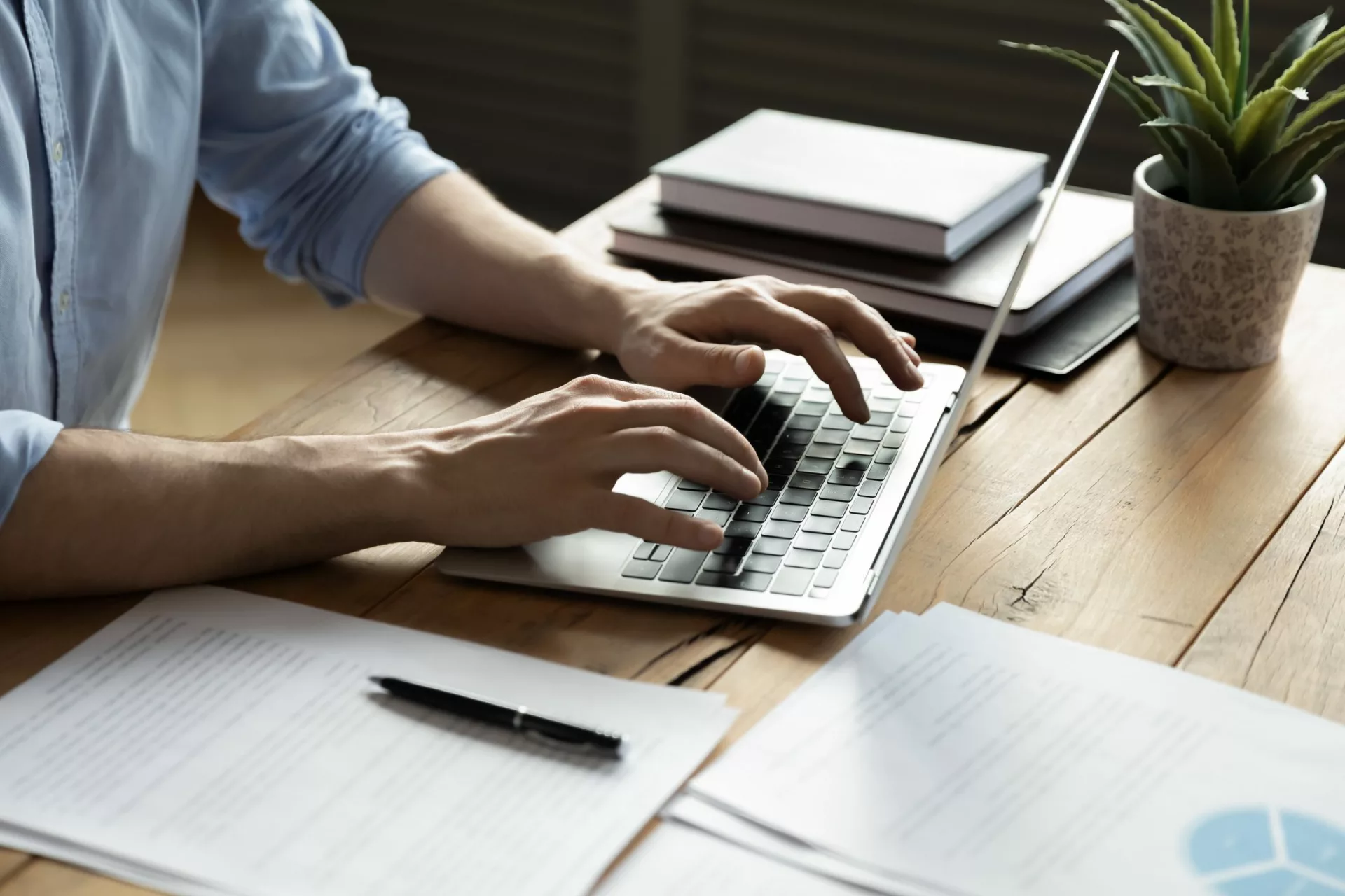 businessman typing on laptop with printed documents nearby