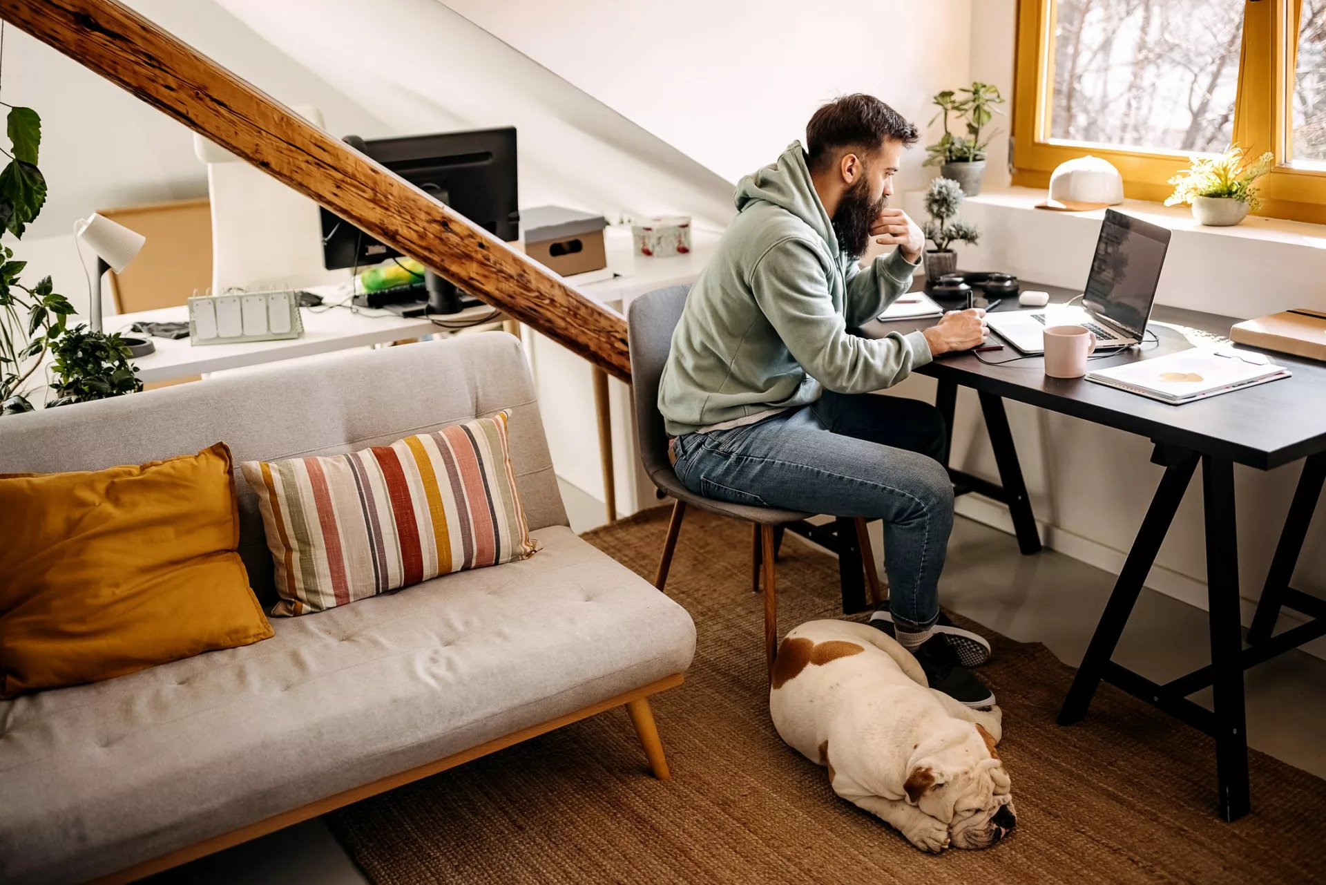 man using remote work software on laptop with dog sleeping nearby