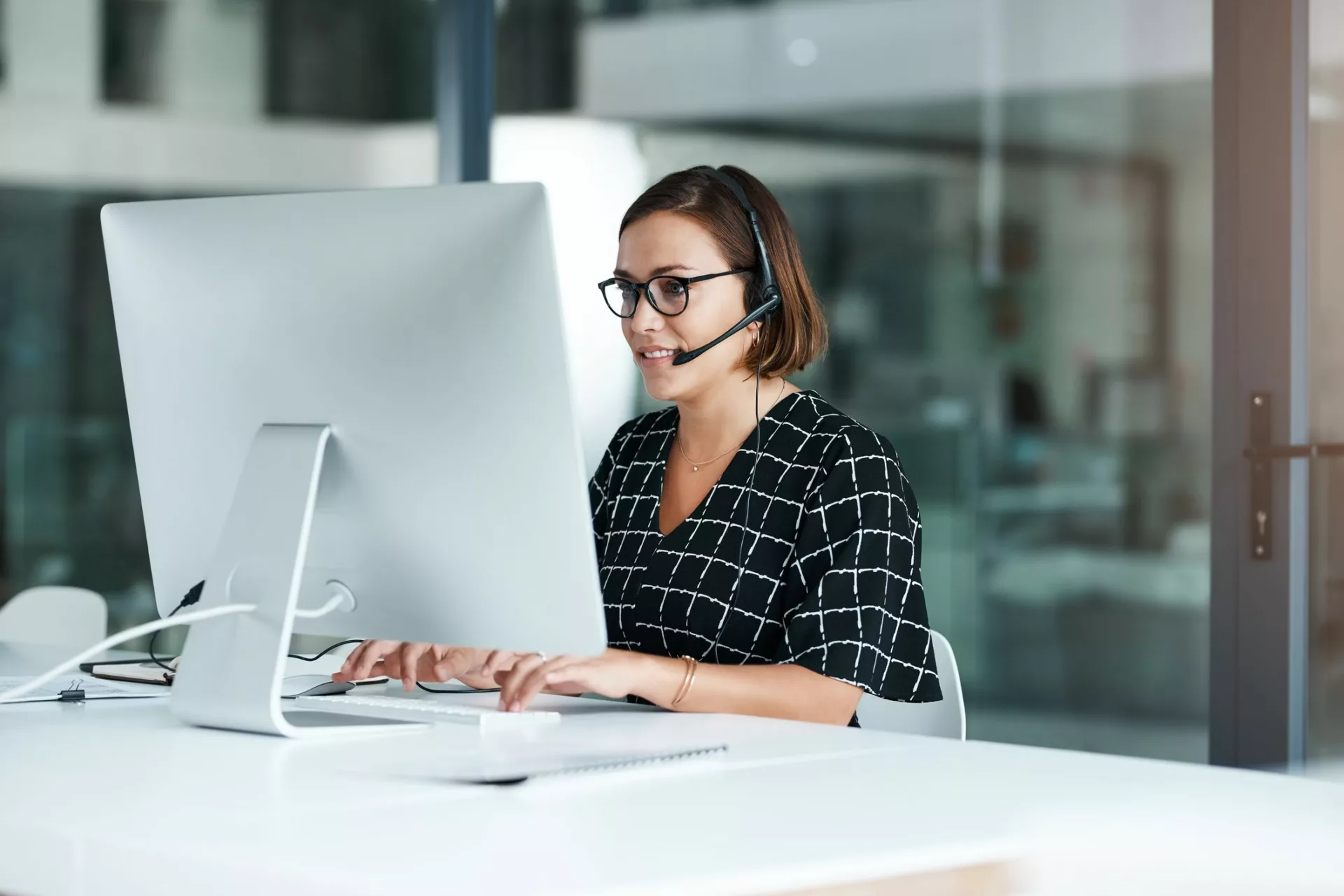 Women with headset looking up information on desktop to demonstrate differences in Bloomfire vs. Salesforce Knowledge