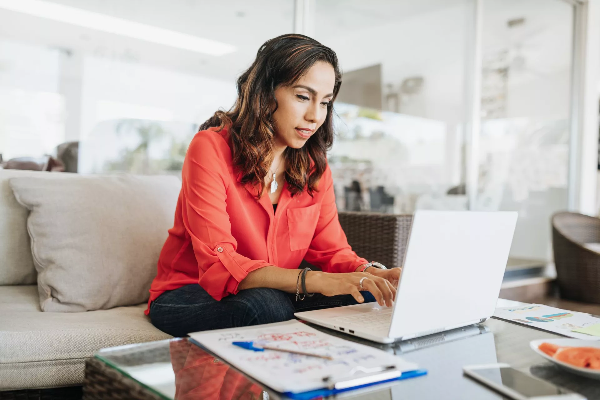 woman in red shirt works on couch in flex work environment