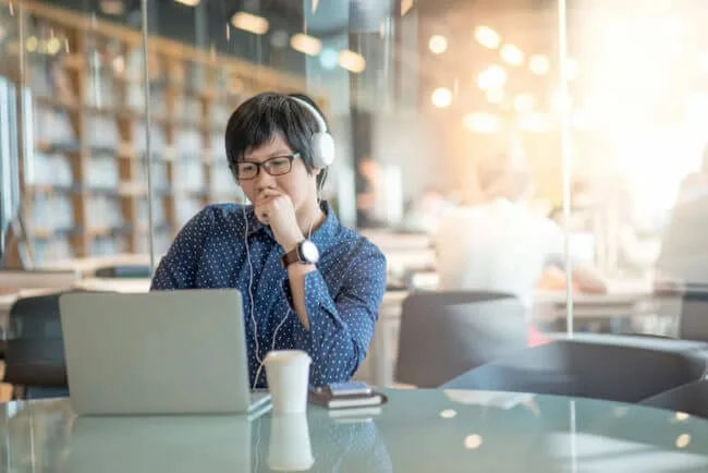 young man on laptop in library browsing customer-facing knowledge base