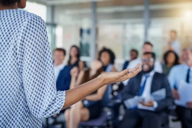 Young woman presenting to group of senior leaders to get executive buy-in for knowledge sharing platform