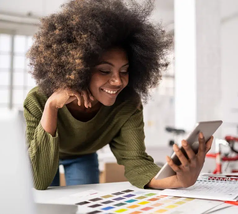 Woman smiling, leaning on desk looking at tablet screen.