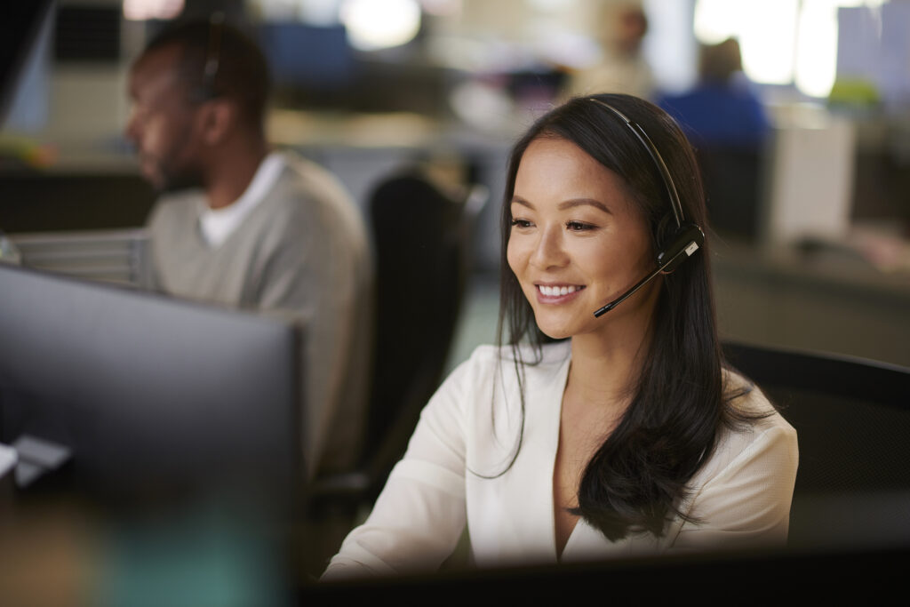 Woman working in call center with headset on smiling at computer screen.