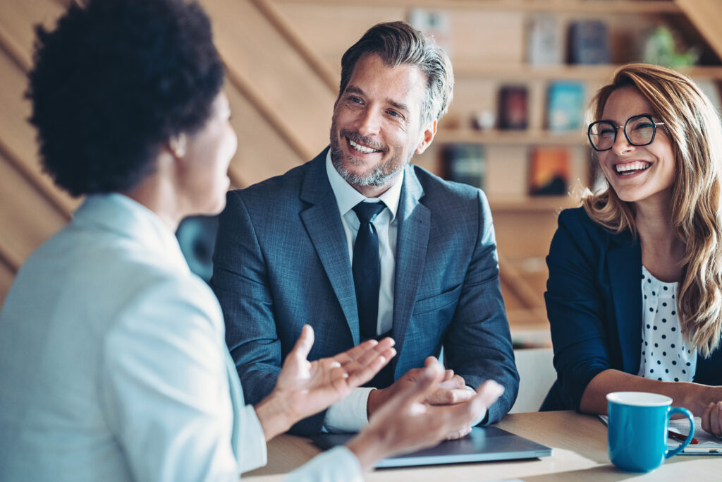 Three business executives in conference room smiling and talking.