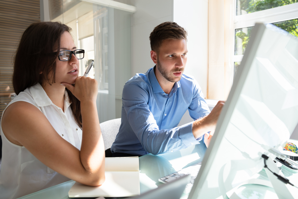 Two employees looking at a computer screen and navigating a platform that presents common knowledge management challenges.