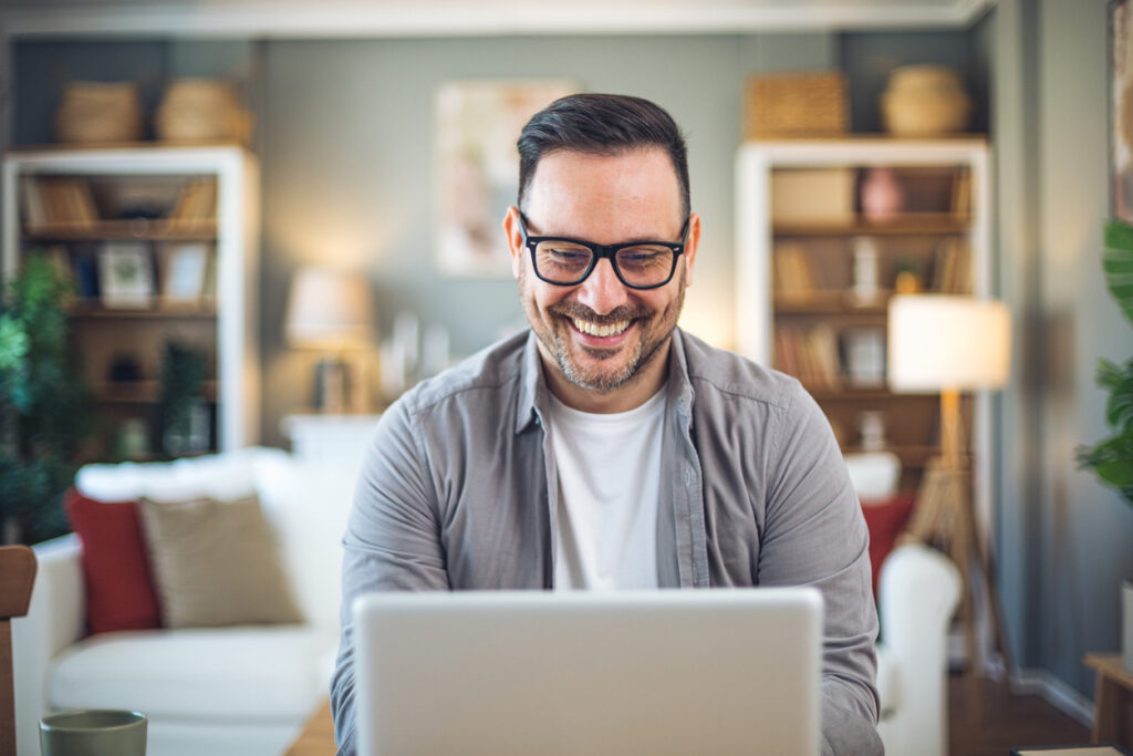 A man smiling in front of a laptop as he finds the answer to the question: how does AI enterprise search work