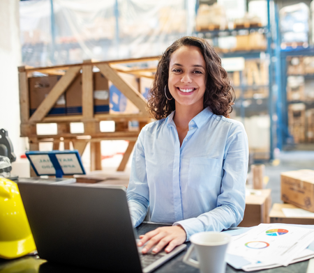 Smiling woman in warehouse at laptop